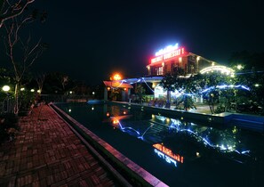 A hotel with a pool, illuminated signage, and a bridge over the water.