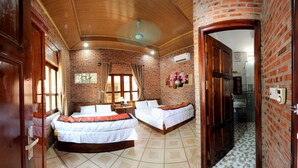 Una habitación con dos camas, una pared de ladrillo, techo de madera y suelo de baldosas.