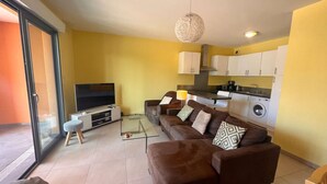 A living room with a sofa, a coffee table, a TV, and a kitchen area with cabinets and appliances.