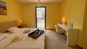 A hotel room with a bed, a desk, a chair, a balcony, and a painting on the wall.