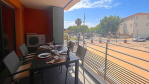 A balcony with a table set for dining, overlooking a street with buildings and trees.