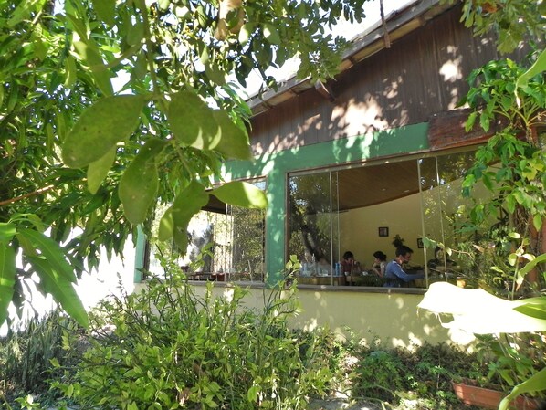 A building with a large glass window, surrounded by greenery. - Pousada Éden Águas Termais (Colinas do Sul)