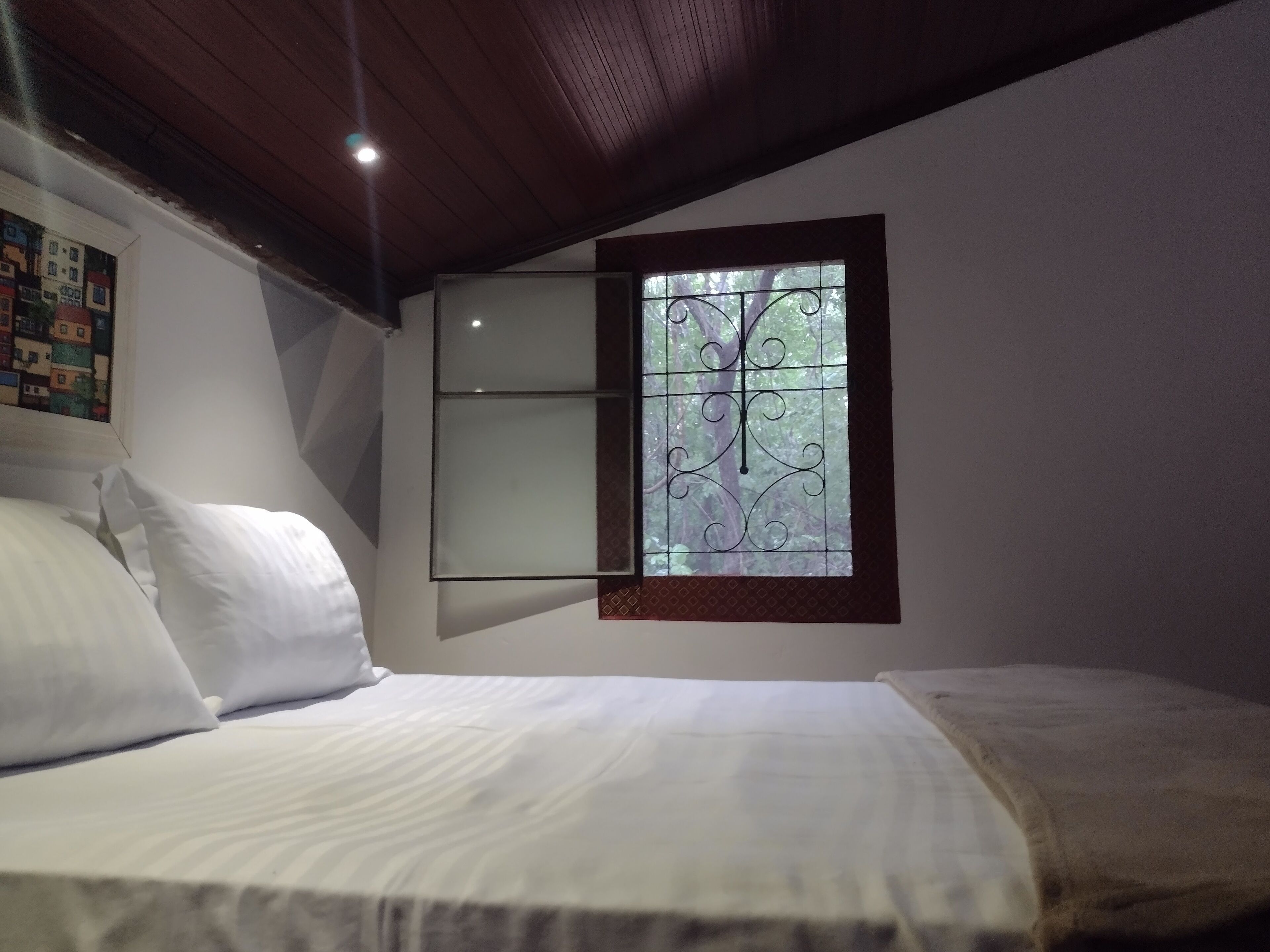 A bedroom with a bed, a window with a decorative metal grille, and a wall-mounted shelf.