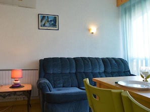 A room with a blue sofa, a small table with a glass and plate, a lamp, and a painting on the wall.
