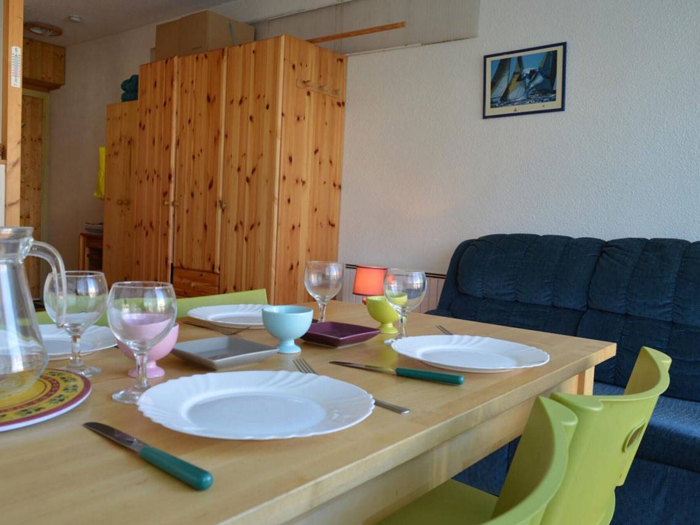 A dining table set with plates, glasses, and cutlery, a pitcher, and a lamp.