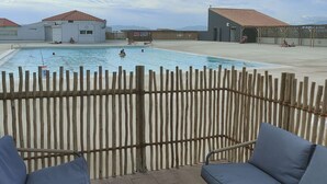 A swimming pool area with a wooden fence, lounge chairs, and buildings in the background. - Elevated Ground Floor Apartment, 3 Rooms, 6 Sleeps, Pool, Terrace, Parking, Sports Facilities (Port Barcarès)