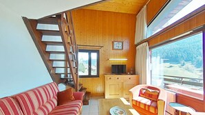 Ein gemütliches Wohnzimmer mit einer Holztreppe, einem Sofa, einem Couchtisch und Blick ins Freie.