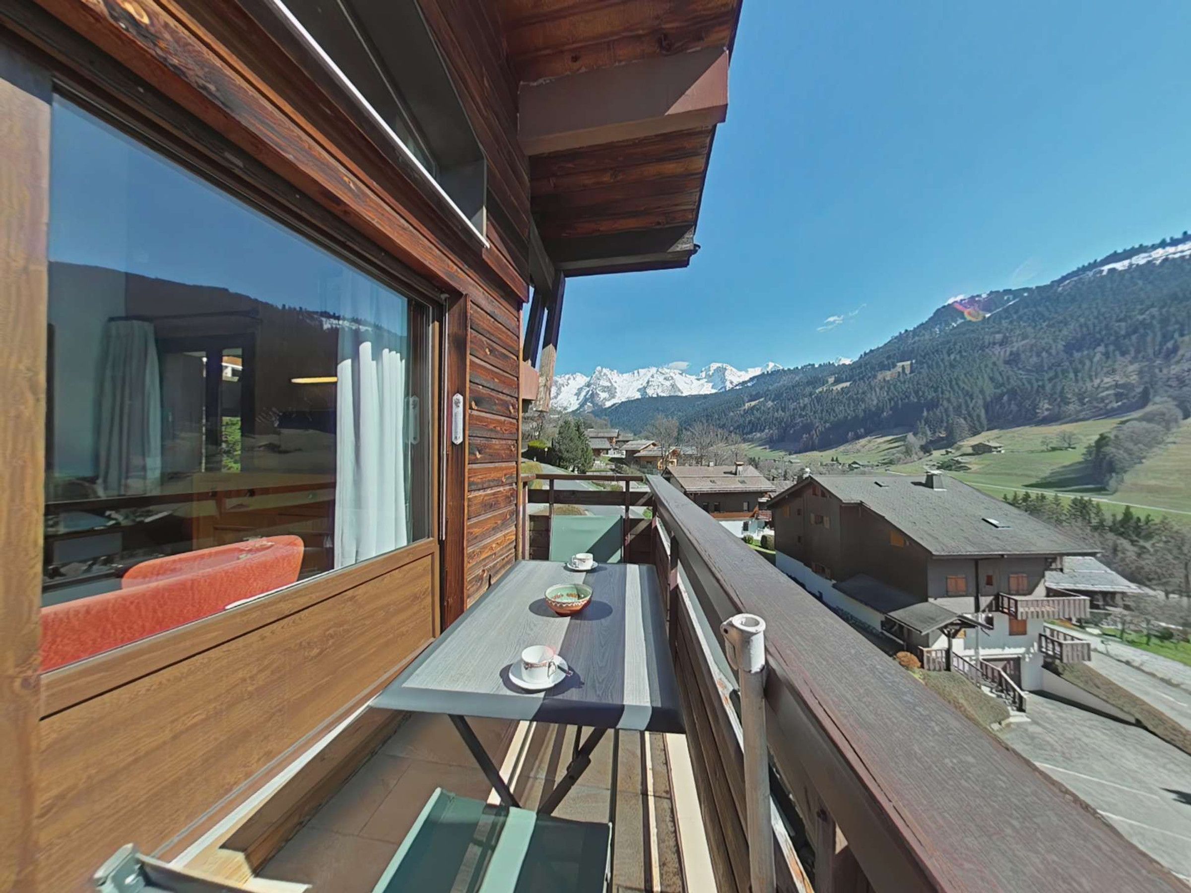 A wooden balcony with a table and chairs, overlooking a mountainous landscape.