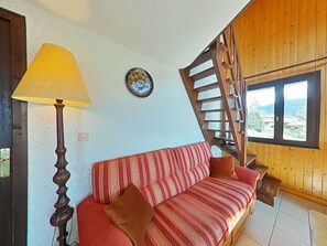 Une pièce chaleureuse avec un escalier en bois, un canapé agrémenté de coussins à rayures, une lampe et une assiette décorative accrochée au mur.