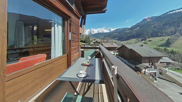 Ein Holzbalkon mit Tisch und Stühlen, mit Blick auf eine Berglandschaft.
