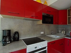 Una cocina con armarios rojos, una estufa negra, una cafetera y un microondas.