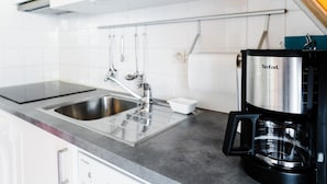 Una cocina con un lavamanos de acero inoxidable, una cafetera negra y un microondas sobre la encimera.