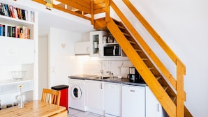 Una cocina compacta con armarios blancos, un microondas, un lavamanos y una escalera de madera.