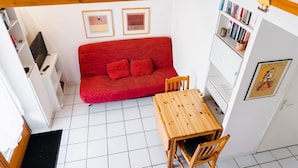 Una habitación acogedora con un sofá rojo, una mesa de madera y una estantería.