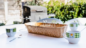 Una mesa servida con tazas blancas, una cesta de mimbre y una cuchara.