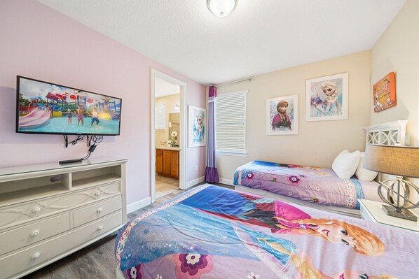 A bedroom with two beds, a TV, a dresser, and a bathroom visible through an open door. - 10 min to Disney, private pool home on luxury resort, brand new hardwood floors. (kissimmee)