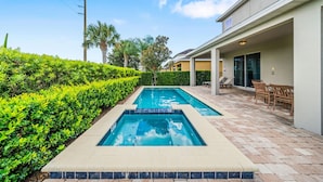 A swimming pool with two separate sections, surrounded by well-maintained hedges and a patio area with chairs. - 10 min to Disney, private pool home on luxury resort, brand new hardwood floors. (kissimmee)