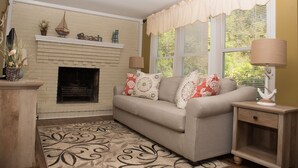 A living room with a fireplace, a sofa with decorative pillows, a wooden side table, and a patterned rug.