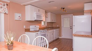 A compact kitchen with white cabinets, a microwave, a stove, and a refrigerator. There is a dining table with chairs and a small plant on the table.