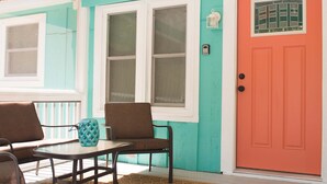 A covered porch with a table and chairs, a red door, and decorative fish on the wall.