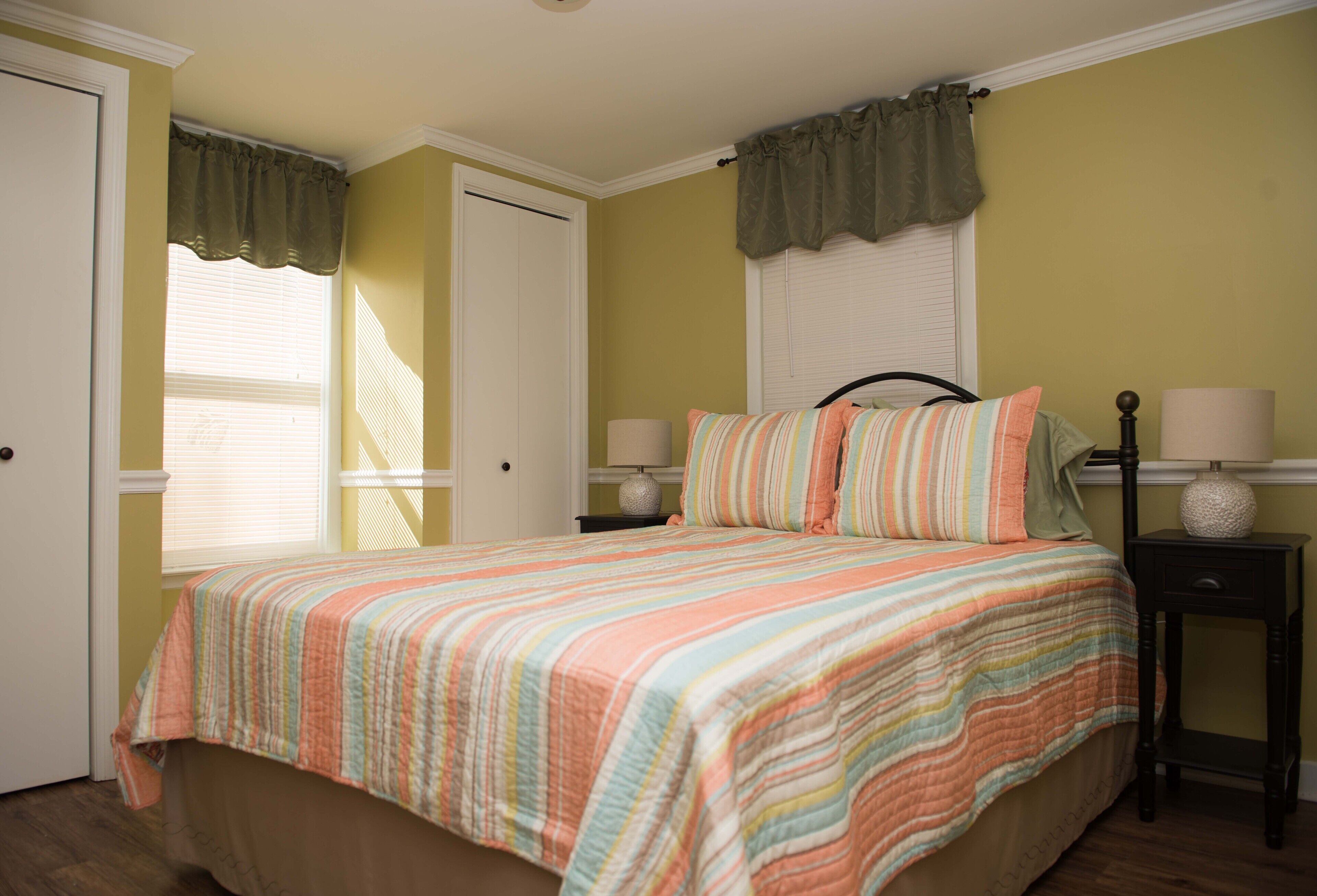 A bedroom with a bed, two bedside tables, a window with curtains, and a door.