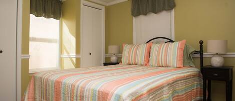 A bedroom with a bed, two bedside tables, a window with curtains, and a door.
