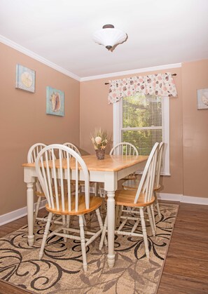 A dining room with a wooden table and white chairs, a decorative ceiling light, and a window with blinds.