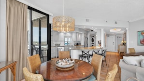 A modern kitchen with white cabinets, a dining area with wicker chairs, and a large window.