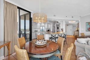A modern kitchen with white cabinets, a dining area with wicker chairs, and a large window.