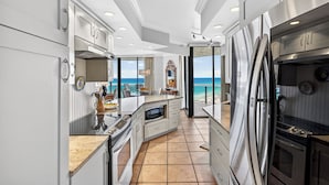 A modern kitchen with a view of the ocean, featuring stainless steel appliances, white cabinetry, and a large island with a built-in oven.
