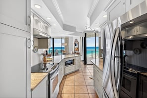 A modern kitchen with a view of the ocean, featuring stainless steel appliances, white cabinetry, and a large island with a built-in oven.