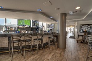 A bar area with wooden flooring, bar stools, and a counter with a television displaying a sports game.