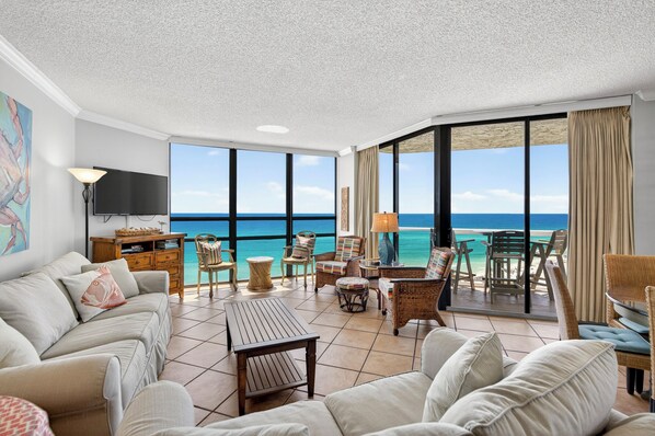 A spacious living room with a large TV, comfortable seating, and a balcony with a view of the ocean.