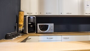 A modern kitchen with white cabinets, a coffee machine, a microwave, and two stools. - Ciccio B&B (Bergamo)