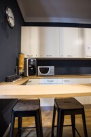 Una cucina moderna con mobili bianchi, una macchina da caffè, un forno a microonde e due sgabelli.