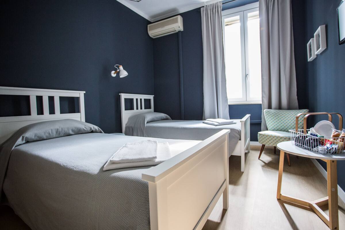 Une chambre avec deux lits, une table de chevet, une chaise et une fenêtre avec des rideaux.