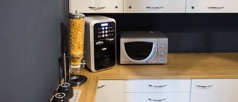 A compact kitchen with white cabinets, a microwave, a coffee machine, and a clock on the wall.