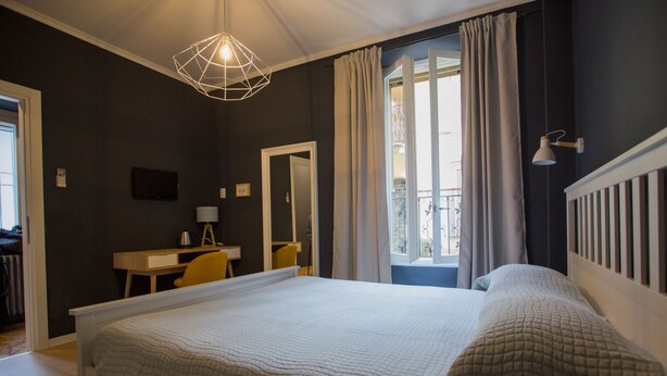 A bedroom with a large bed, a desk, a chair, a mirror, and a window with curtains. - Ciccio B&B (Bergamo)