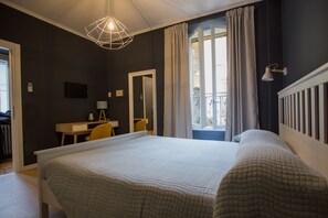 A bedroom with a large bed, a desk, a chair, a mirror, and a window with curtains. - Ciccio B&B (Bergamo)