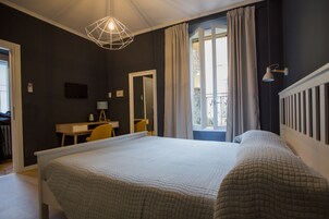 Una camera da letto con un letto grande, una scrivania, una sedia, uno specchio e una finestra con tende.