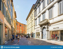 Una strada pedonale fiancheggiata da edifici storici, negozi e un cielo sereno.