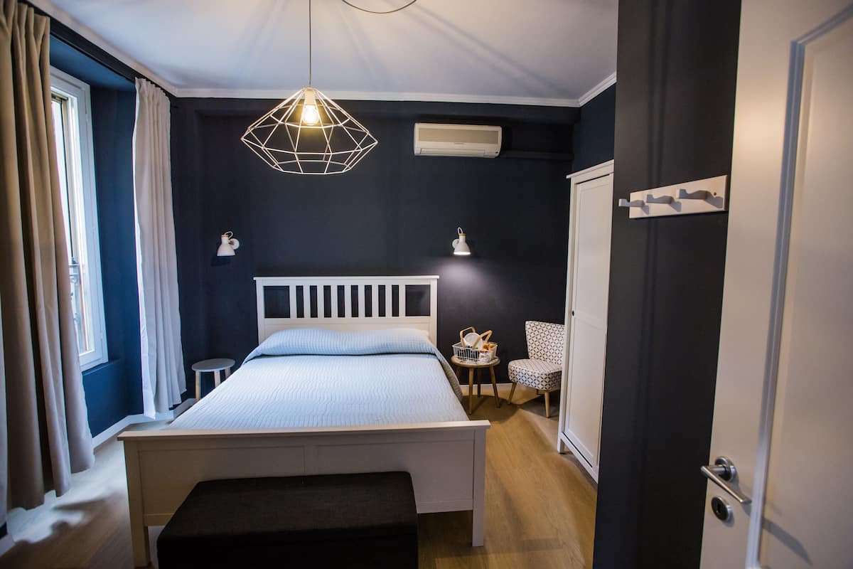 Une chambre à coucher comprenant un lit, des tables de chevet, une chaise, un luminaire suspendu et une porte.