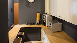 A compact kitchen with a wooden countertop, a coffee machine, and a microwave. There are two stools and a clock on the wall. - Ciccio B&B (Bergamo)
