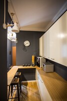 Una cucina compatta con un piano di lavoro in legno, una macchina da caffè e un forno a microonde. Ci sono due sgabelli e un orologio appeso al muro.