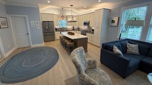 A modern kitchen with a central island, bar stools, and a dark blue sofa in a living area.