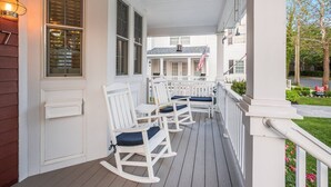 A porch with white rocking chairs and a white railing.