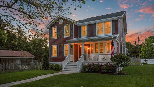 A two-story house with a front porch, a picket fence, and a well-maintained lawn.