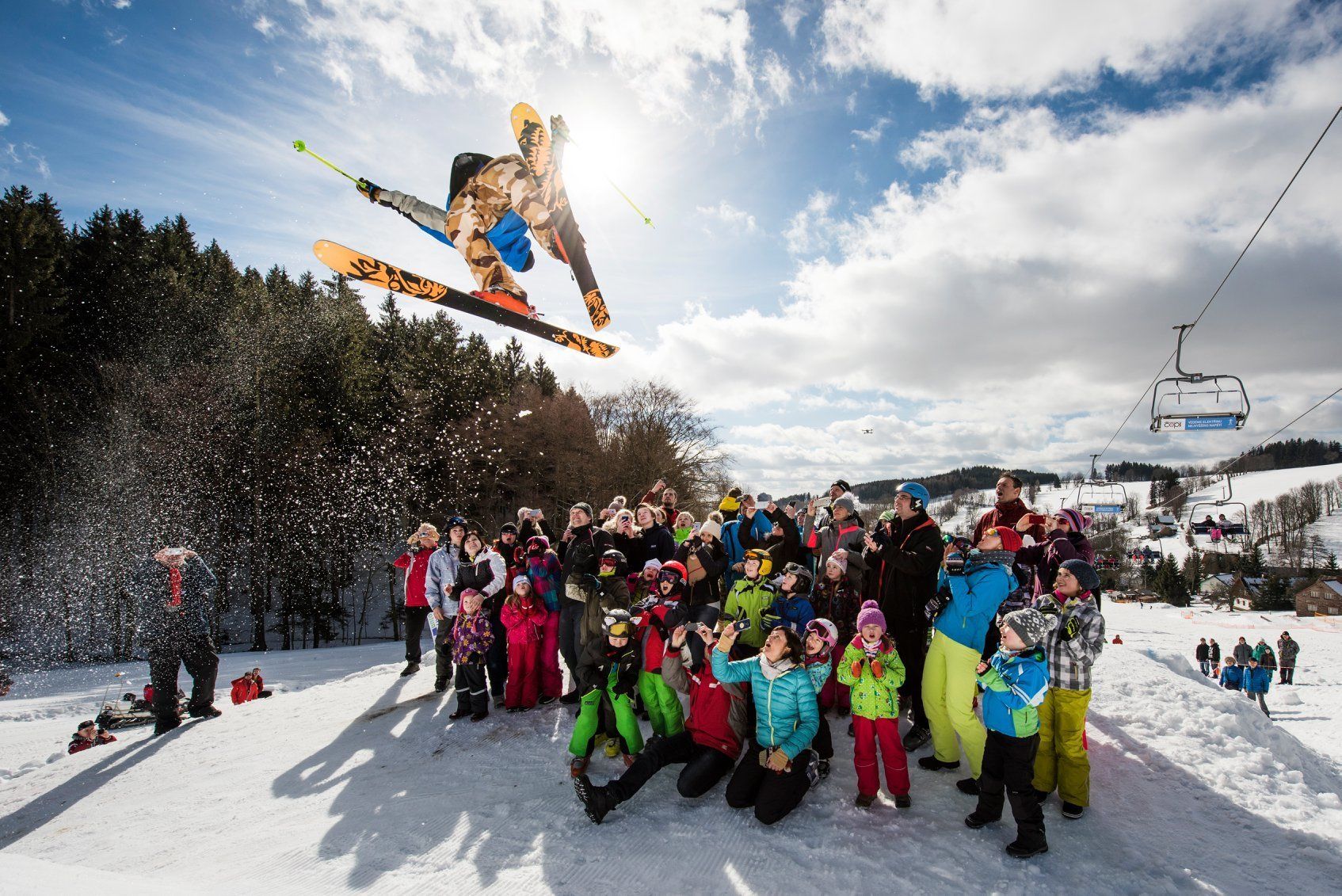 Een groep mensen verzameld op een besneeuwde helling, met een skilift op de achtergrond.