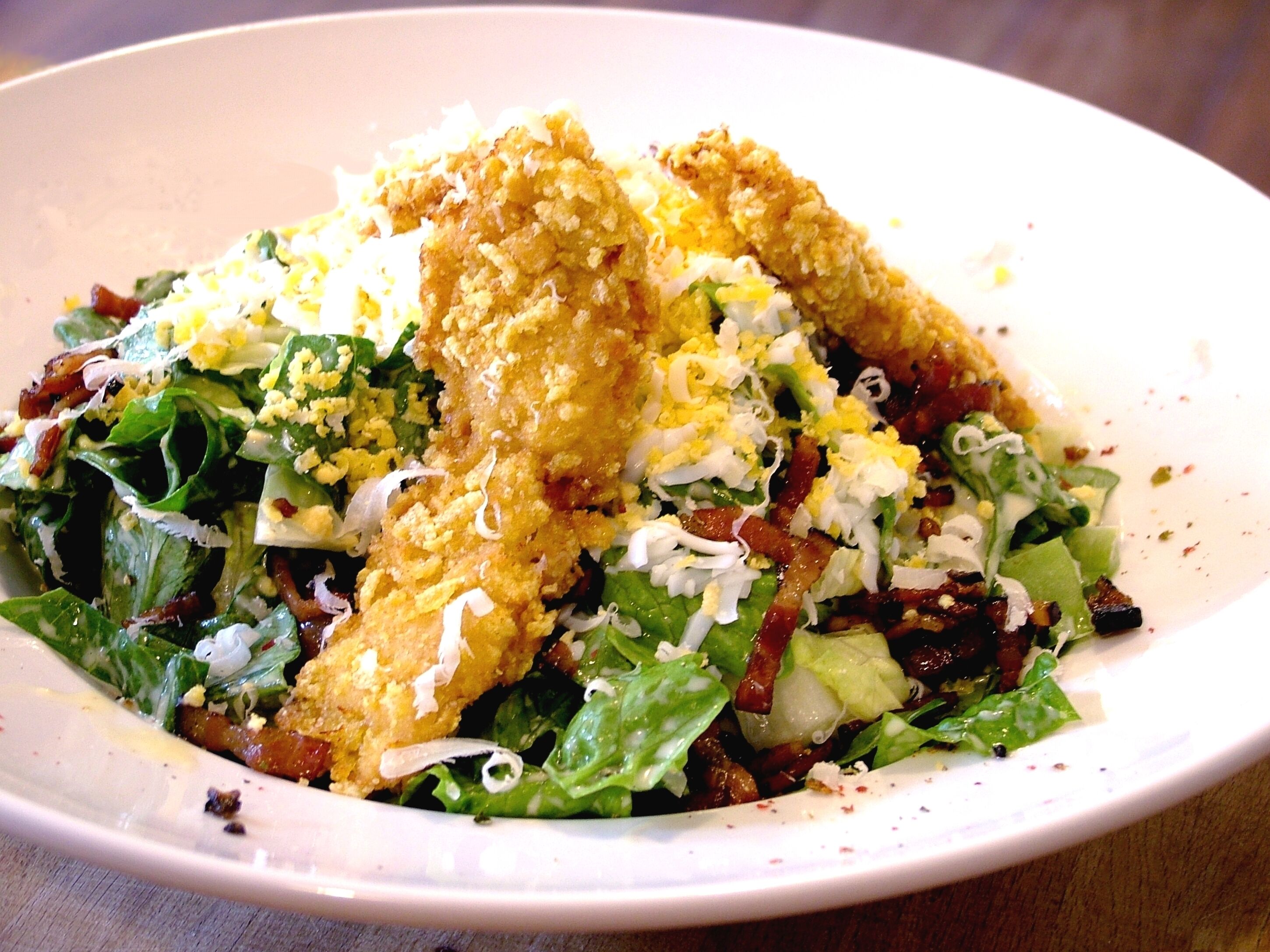A plate of food with a salad, bacon, and fried items.