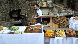 Een buitenbarbecue met een steenoven, een grill en verschillende etenswaren op tafels.
